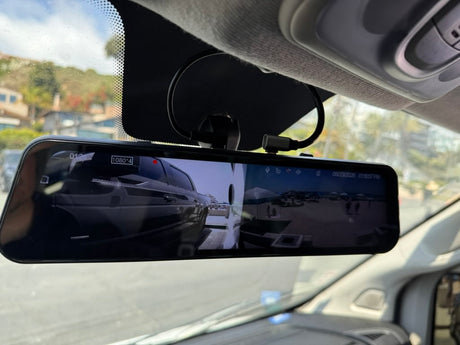 Digital rearview mirror in an RV rental, displaying a split screen view: a front vehicle perspective and a beach scene.