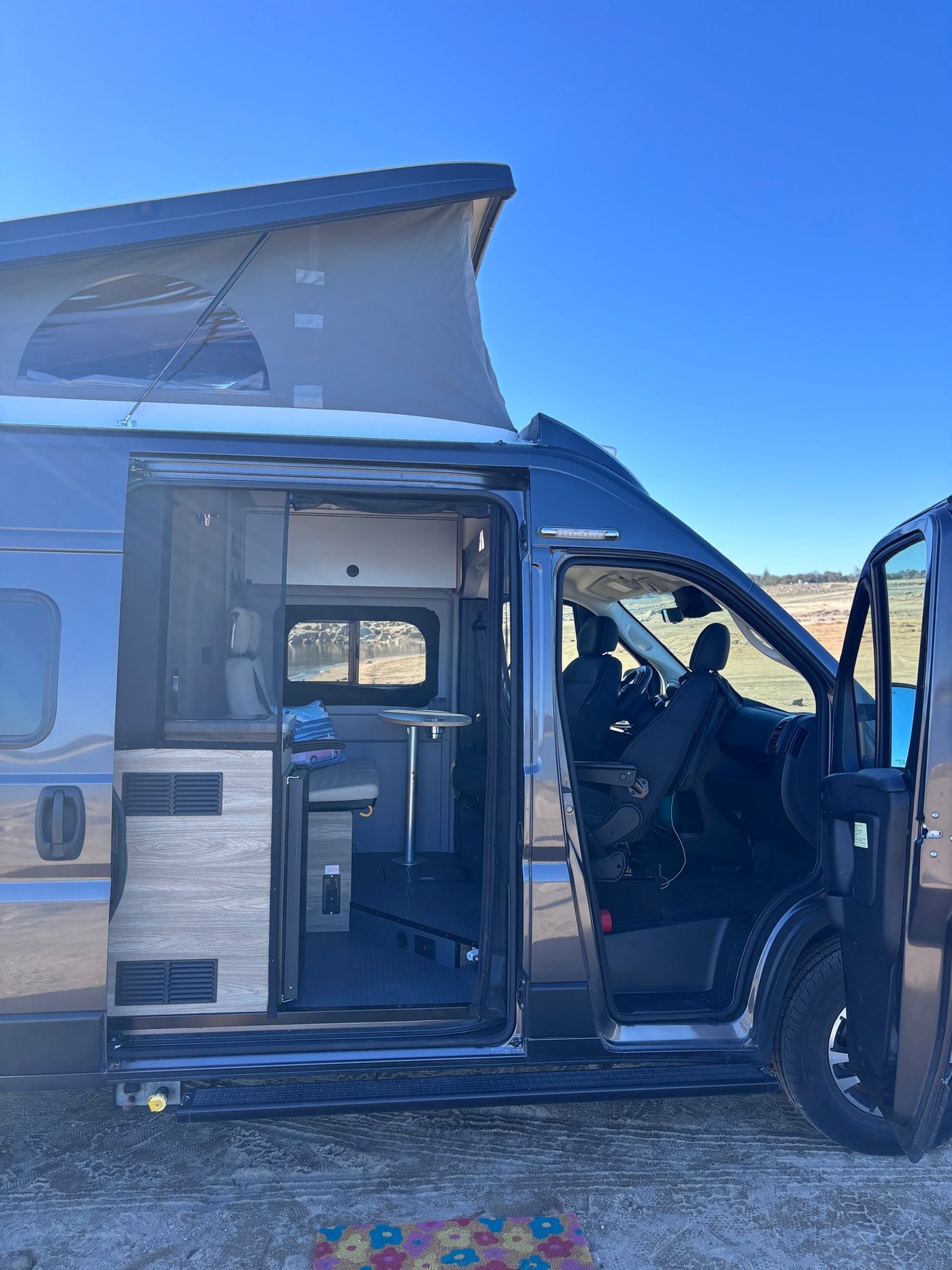 Modern grey pop-top camper van rv rental. Open doors reveal cozy interior with table, seating, and front cabin view. — photo 15