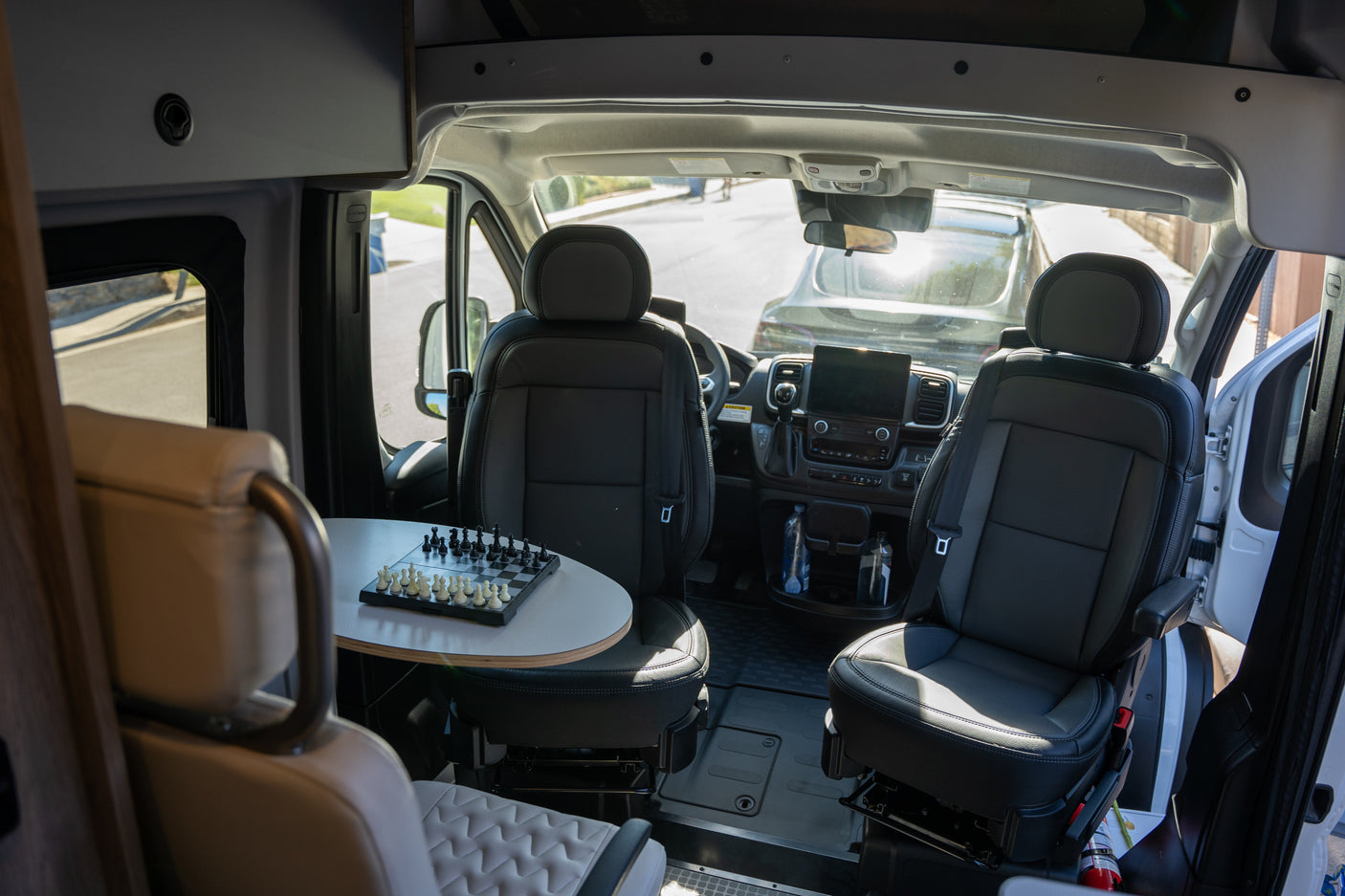 This RV rental interior features swiveling front seats, a table with a chessboard, and a functional cockpit, ready for adventure.