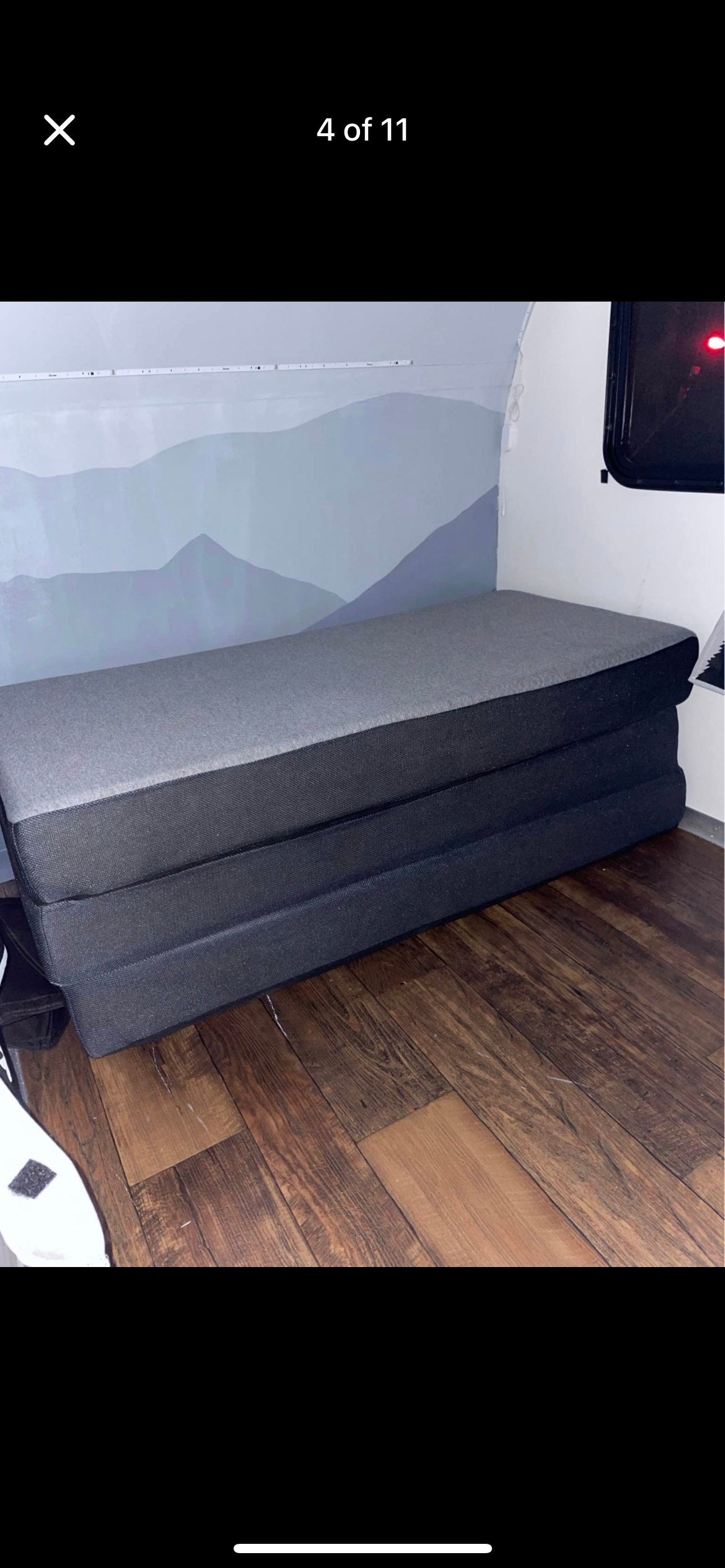 RV rental interior: A gray, three-section foldable mattress on a dark wood floor, set against a light mountain mural wall and strip lighting.
