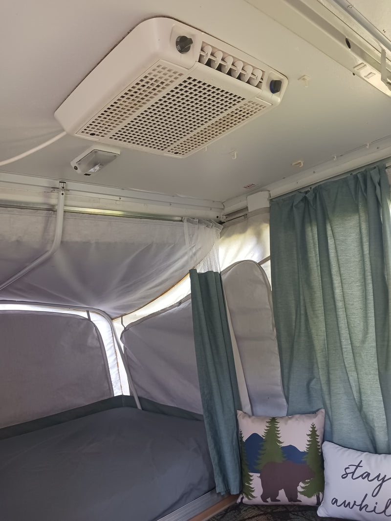 Cozy RV rental interior. Pop-up camper bedroom with a ceiling AC unit, comfy bed, and inviting pillows. — photo 10