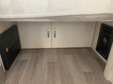 RV rental interior view: power distribution panel, storage cabinets, and an air vent on wood-look flooring.