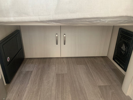 RV rental interior view: power distribution panel, storage cabinets, and an air vent on wood-look flooring.