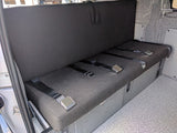 RV rental: Versatile camper van interior showing a dark grey bench seat with three lap seatbelts & built-in storage.