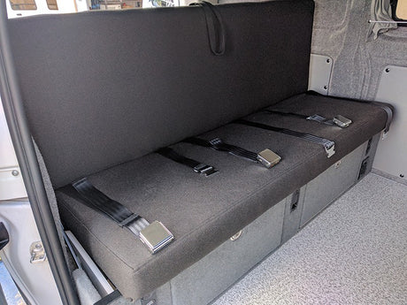 RV rental: Versatile camper van interior showing a dark grey bench seat with three lap seatbelts & built-in storage.