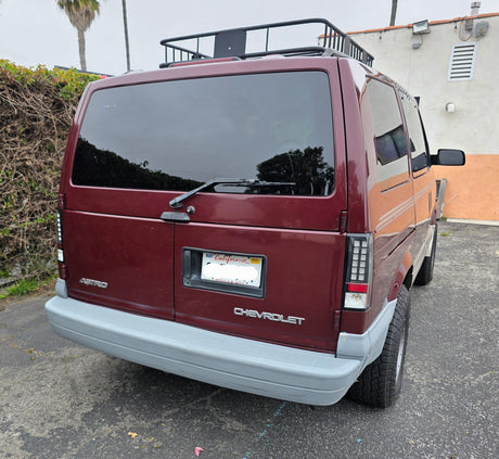 Rear of a maroon Chevrolet Astro van with roof rack & LED taillights. Could be an RV rental for road trips.