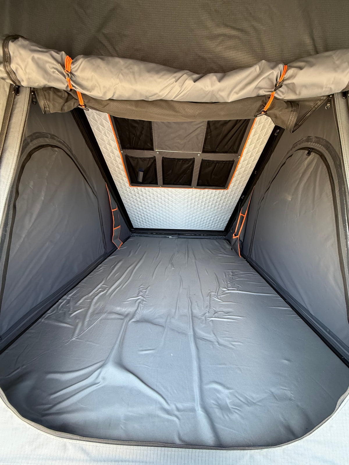 Interior view of an RV rental rooftop tent, featuring a grey sleeping area, quilted ceiling, and storage pockets. — photo 7