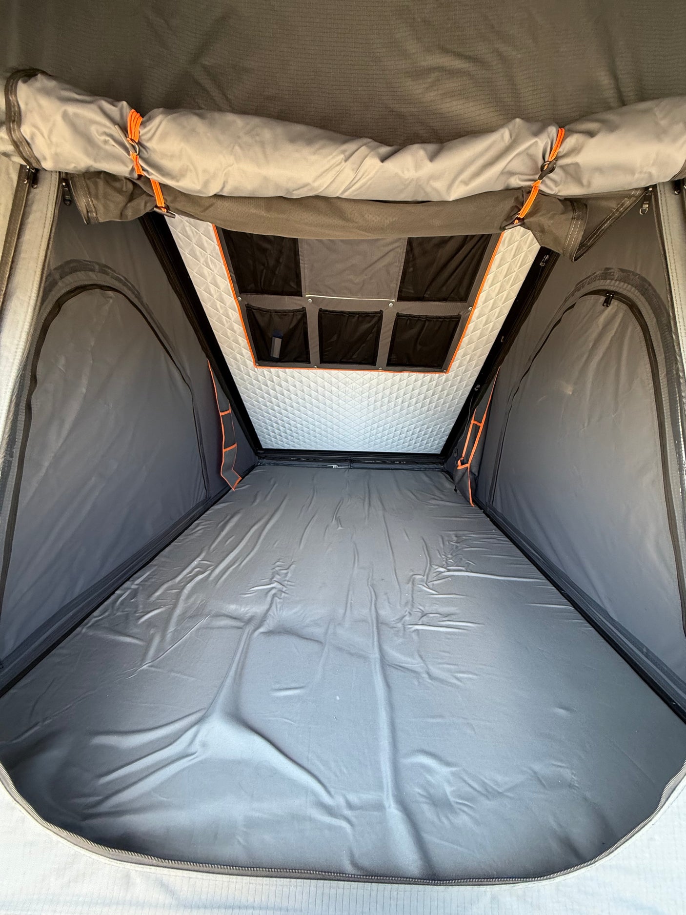 Interior view of an RV rental rooftop tent, featuring a grey sleeping area, quilted ceiling, and storage pockets.