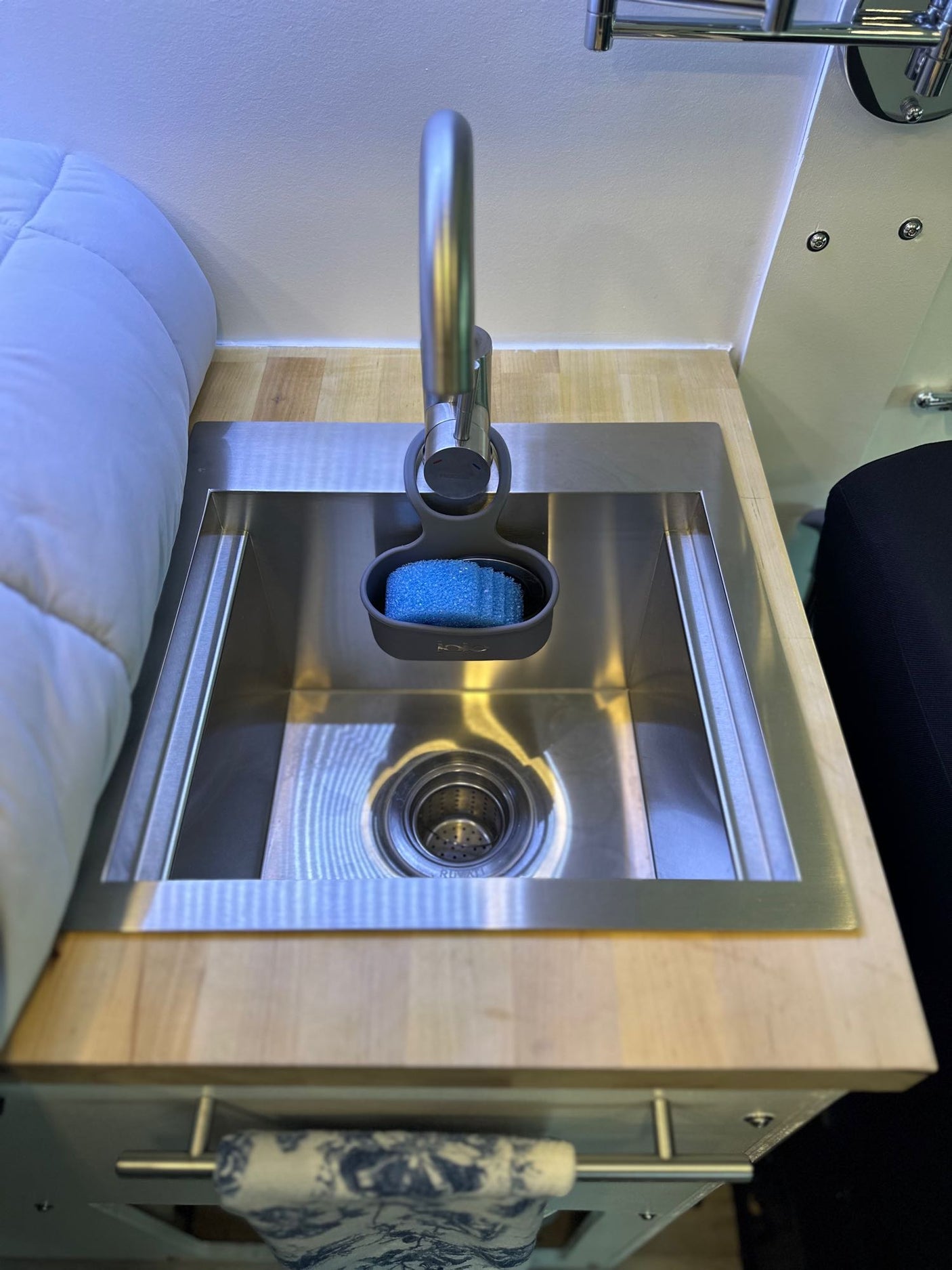 Compact kitchen sink area in an RV rental, featuring a stainless steel basin, modern faucet with sponge, and wooden countertop.