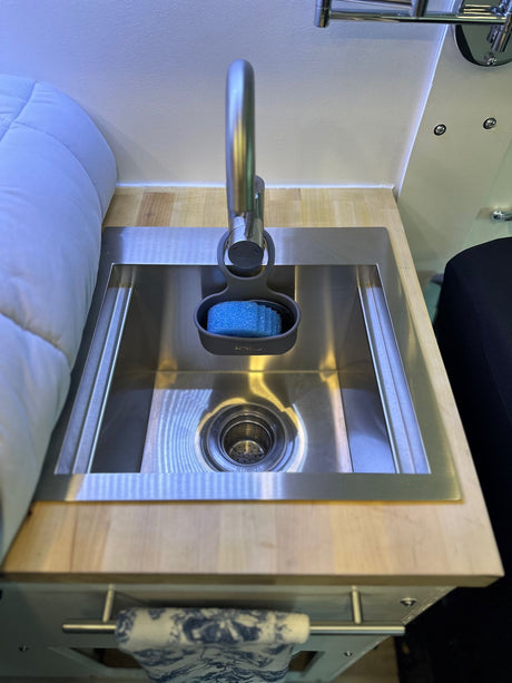 Compact kitchen sink area in an RV rental, featuring a stainless steel basin, modern faucet with sponge, and wooden countertop.