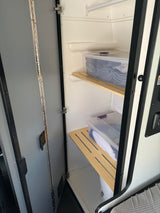 RV rental shower stall converted to storage with slatted shelves holding clear bins of towels and supplies, maximizing space.