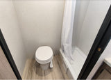 Compact RV rental bathroom with a white toilet on the left and a shower stall with a white curtain on the right.