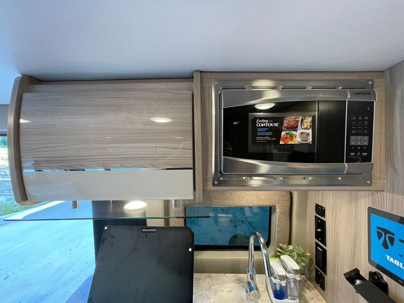 This RV rental kitchen features a sleek Contoure microwave, sink, modern cabinetry, and a tablet display. — photo 12