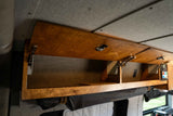 RV rental interior: Open wooden overhead cabinets with gas struts, showing storage, a control panel, and fabric-lined walls.
