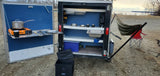 Compact RV rental with an innovative outdoor kitchen featuring a portable stove, pot, sink, and shelves for roadside cooking by the water.