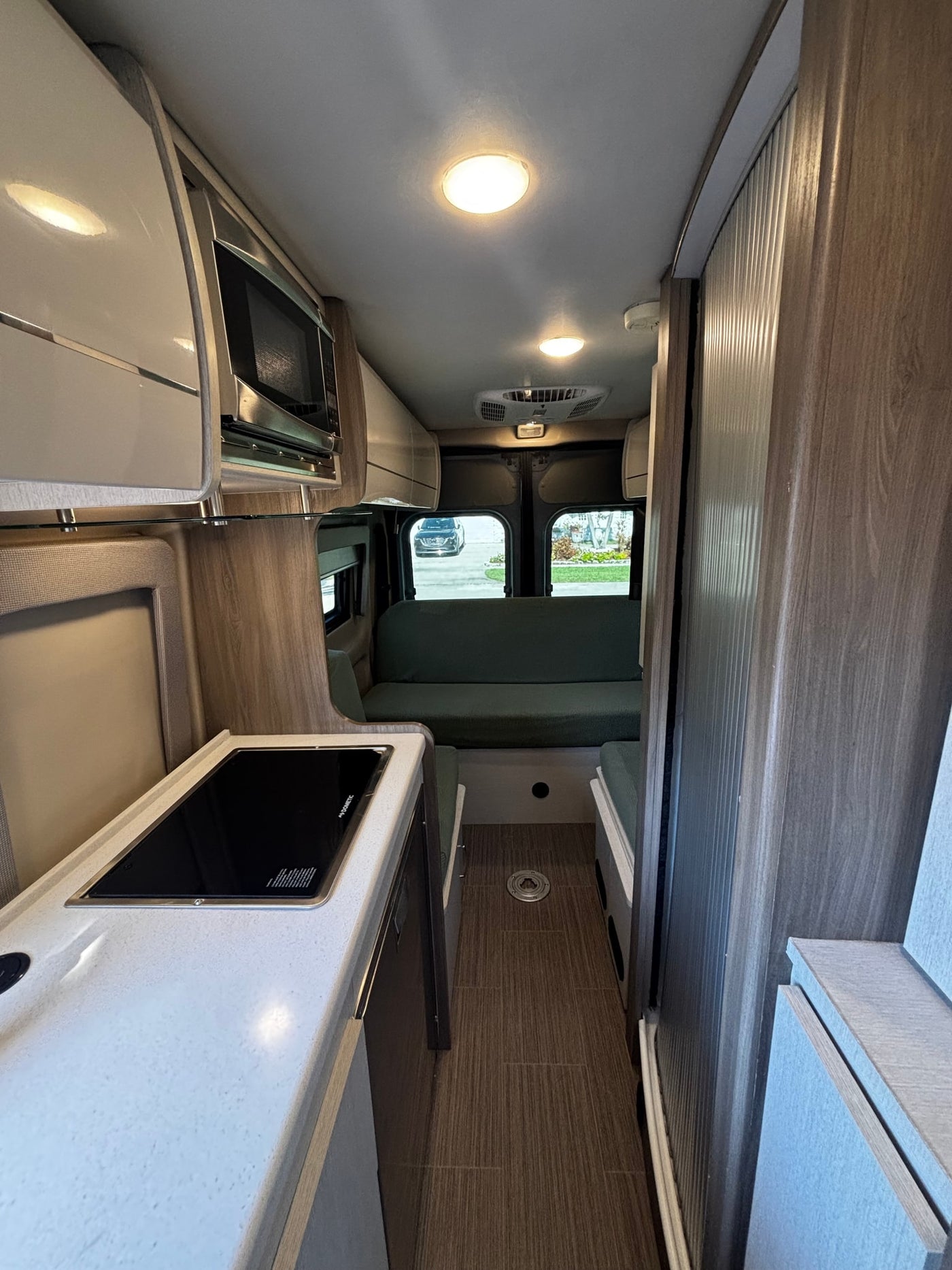 RV rental interior: modern kitchenette with cooktop & microwave, light countertops, and a green sofa, optimizing compact living. — photo 14