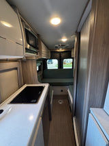 RV rental interior: modern kitchenette with cooktop & microwave, light countertops, and a green sofa, optimizing compact living.