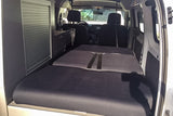 Inside an RV rental: a flexible dark grey bed system unfolds towards the front seats, with sleek storage cabinets on the left.