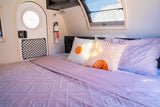 RV rental bedroom featuring a comfy bed with pink bedding, vibrant sun pillows, a round door, and a safety extinguisher.