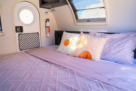 RV rental bedroom featuring a comfy bed with pink bedding, vibrant sun pillows, a round door, and a safety extinguisher.