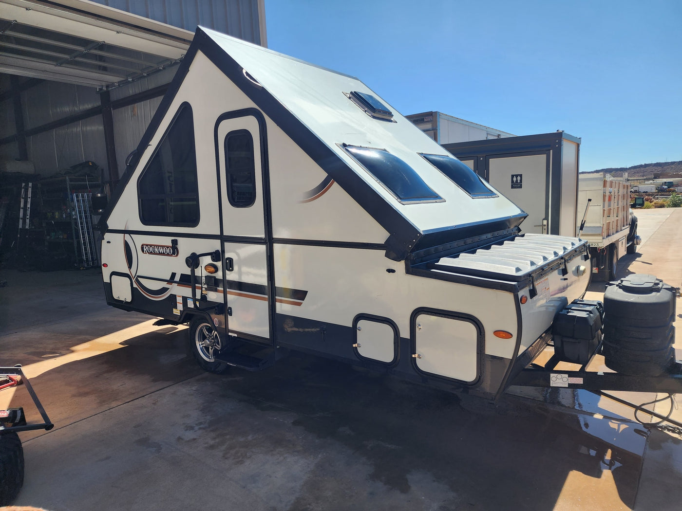 White and dark gray Rockwood A-frame pop-up camper, an RV rental option, parked outdoors with its unique roof & skylights visible. — photo 1