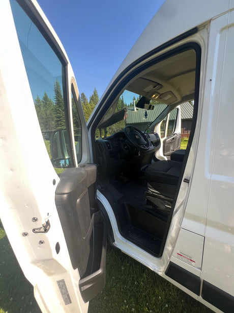 White camper van's open driver's door shows interior cab and forest view. Ideal for your next rv rental trip.