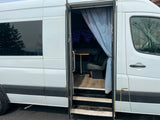 This white RV rental reveals its open side door, showcasing a cozy interior with a table and seating, ready for your next van life adventure.