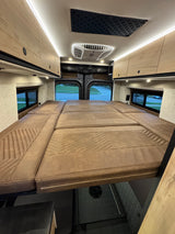 Inside an rv rental: plush bed with geometric stitching, overhead cabinets, and bright lighting for a cozy travel experience.
