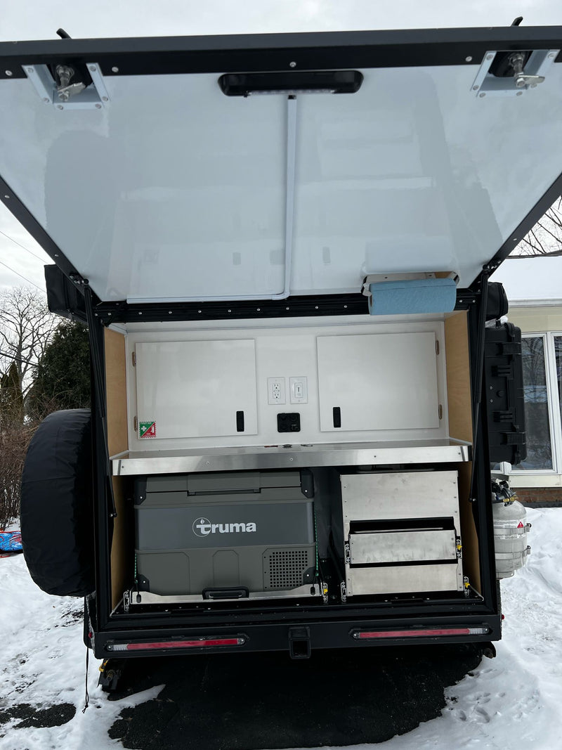  snow-covered for winter adventures.|Overland RV rental trailer's open hatch reveals an outdoor kitchen: Truma fridge — photo 6