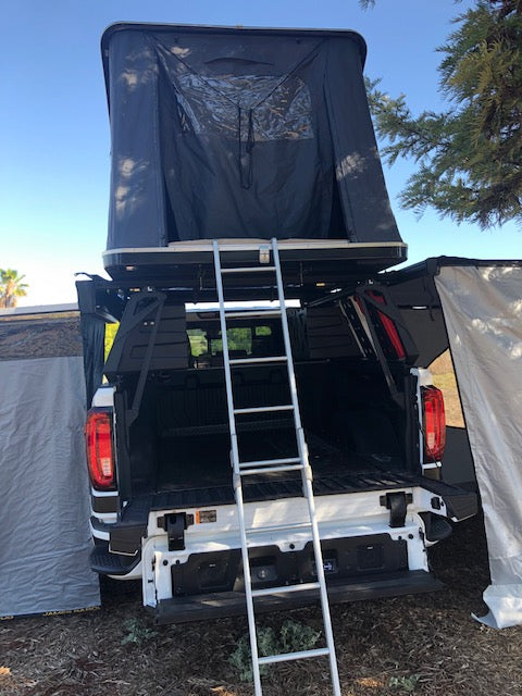 RV rental: White pickup truck with deployed roof-top tent, ladder, and open tailgate for camping.