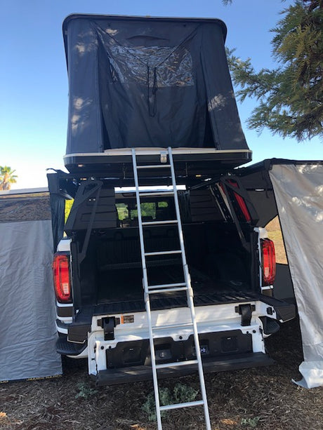 RV rental: White pickup truck with deployed roof-top tent, ladder, and open tailgate for camping.
