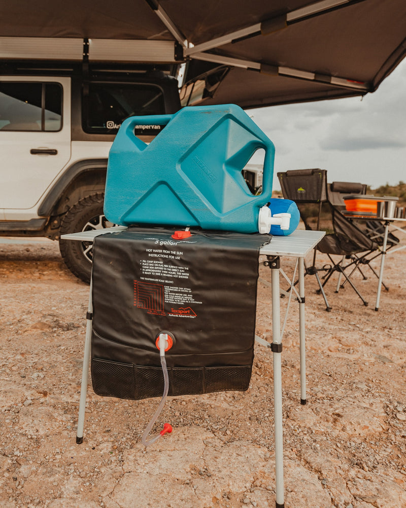 An outdoor camping setup with a solar shower and water jug on a table, beside an RV rental. Ready for a warm camp shower. — photo 20