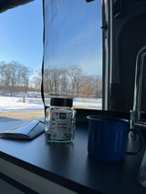 365 Instant Coffee jar and mug in an RV rental, looking out at a peaceful snowy winter landscape.