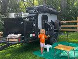 A happy child gives thumbs up next to a rugged Boreas XT camper trailer, ready for an adventure. Perfect for RV rental exploration!