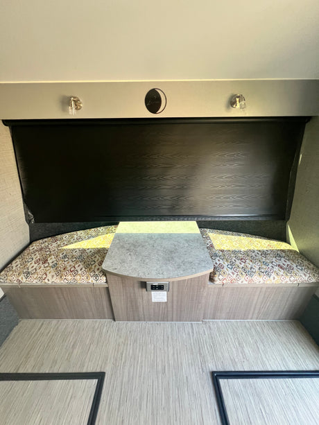 This RV rental dinette features patterned bench seating, a table with power outlets, a dark window shade, and wood-look flooring.
