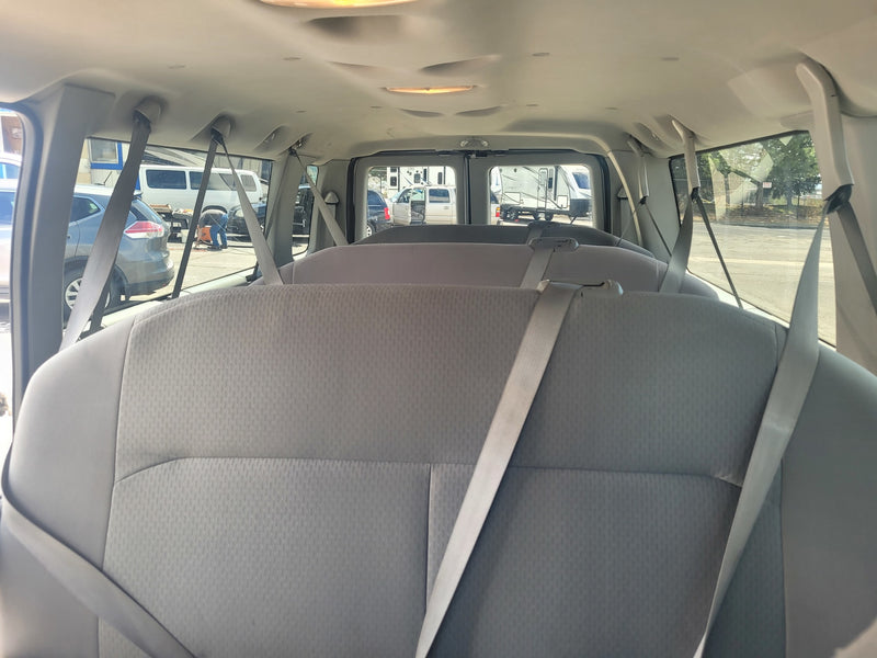 View from inside an RV rental van showing three rows of grey seats and seatbelts, with RVs outside in a sunny parking lot. — photo 5