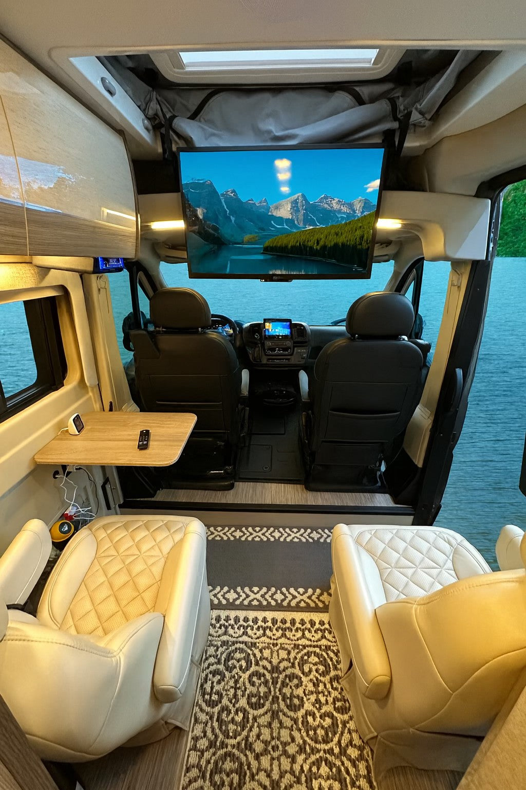 Modern RV rental: cozy interior with comfy seating, TV for entertainment, and a picturesque lake view outside.