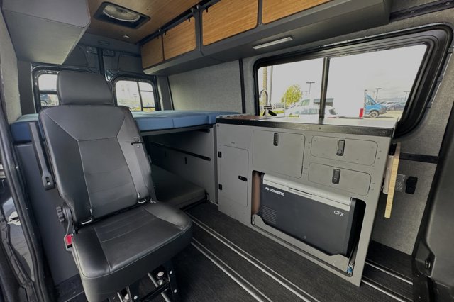  dashboard. Outside view of lot. Adventure awaits.|Experience an RV rental: a cozy camper van interior with a raised blue bed — photo 12