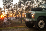 A rugged green Land Rover on a dirt road at sunset, perfect for off-road trips. Find your next adventure, whether it's this or an **RV rental**.