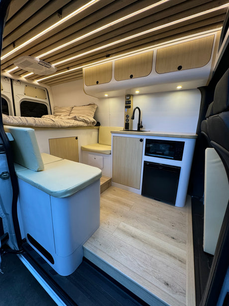 Spacious RV rental interior: modern camper van with kitchen, bed, dinette, and wood accents.