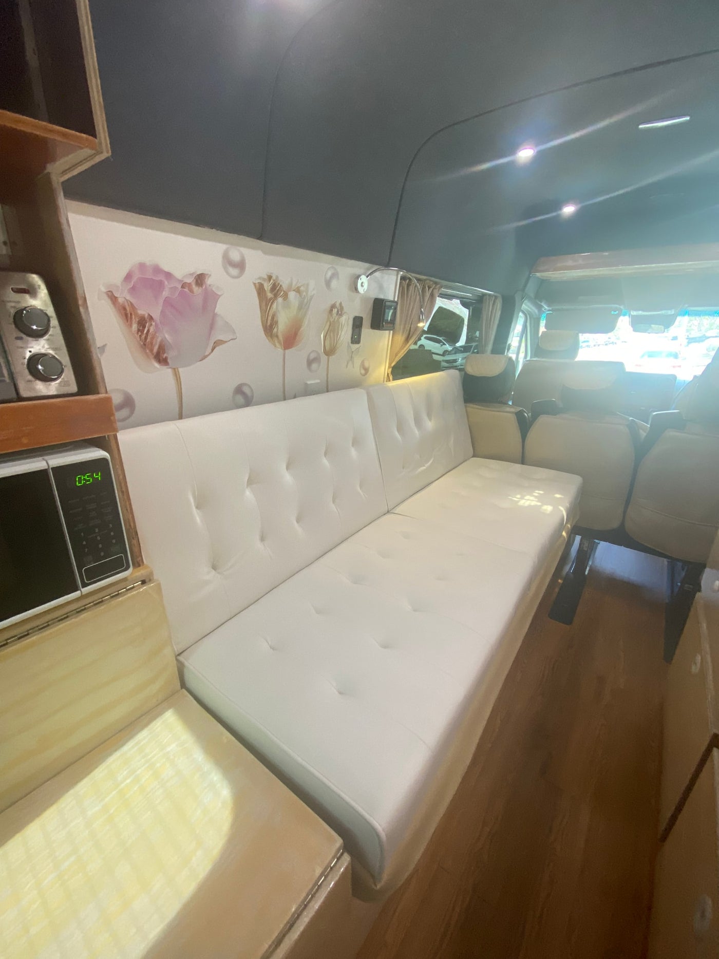 Inside this modern rv rental: a comfy white sofa bed, kitchenette with microwave (0:54), floral walls, & wood floor. Ready for travel! — photo 4