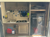 Inside an rv rental, a compact kitchen features a sink, two-burner stove, refrigerator, and smart storage solutions.