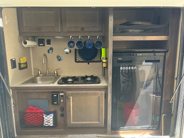 Inside an rv rental, a compact kitchen features a sink, two-burner stove, refrigerator, and smart storage solutions.