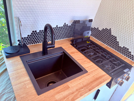 This RV rental features a modern kitchenette with a black sink, faucet, gas stove, wood counter, and unique penny tile backsplash.