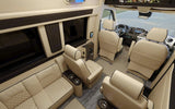 Spacious, luxurious RV rental interior with cream leather seating, integrated entertainment, and modern controls for ultimate comfort.