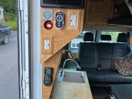 RV rental: Camper van interior with battery monitor, power outlets, kitchen sink, and rear seating for comfortable travels.