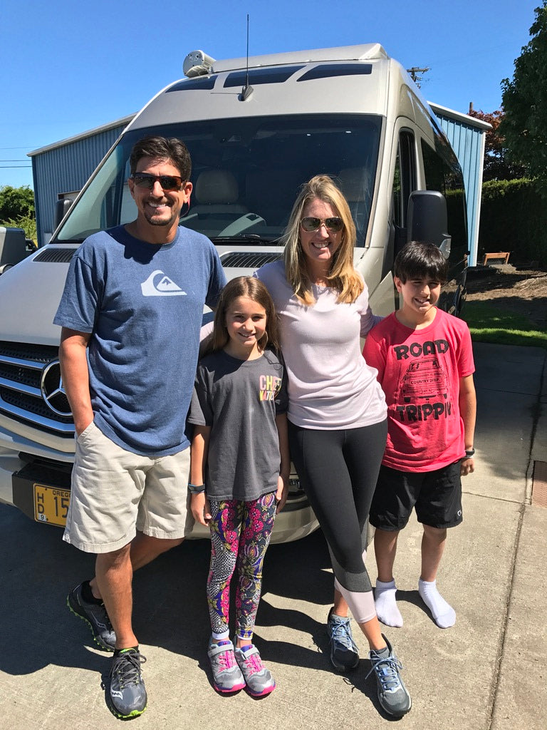 Happy family of four smiles in front of their RV rental, ready for a memorable travel adventure.