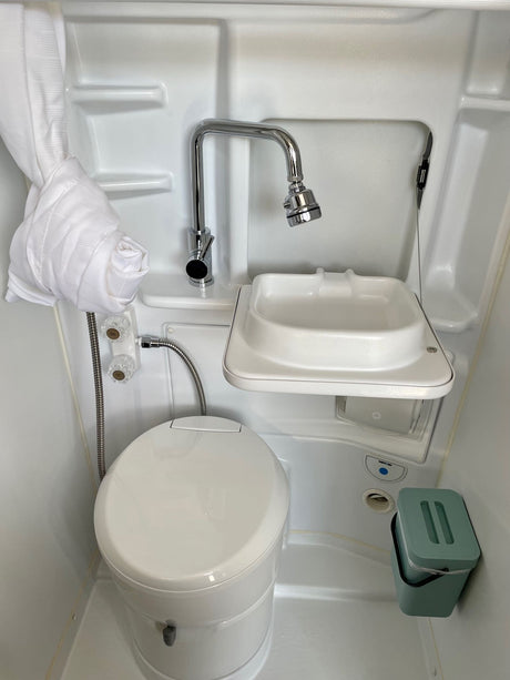 Compact RV rental bathroom with an integrated toilet, small sink, and shower, showcasing efficient design.