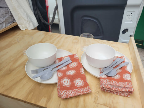 RV rental dining setup: two full place settings, with bowls, plates, cutlery, and sun-patterned napkins on a wooden table.