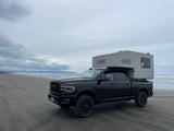 A black Ram truck with a Scout camper